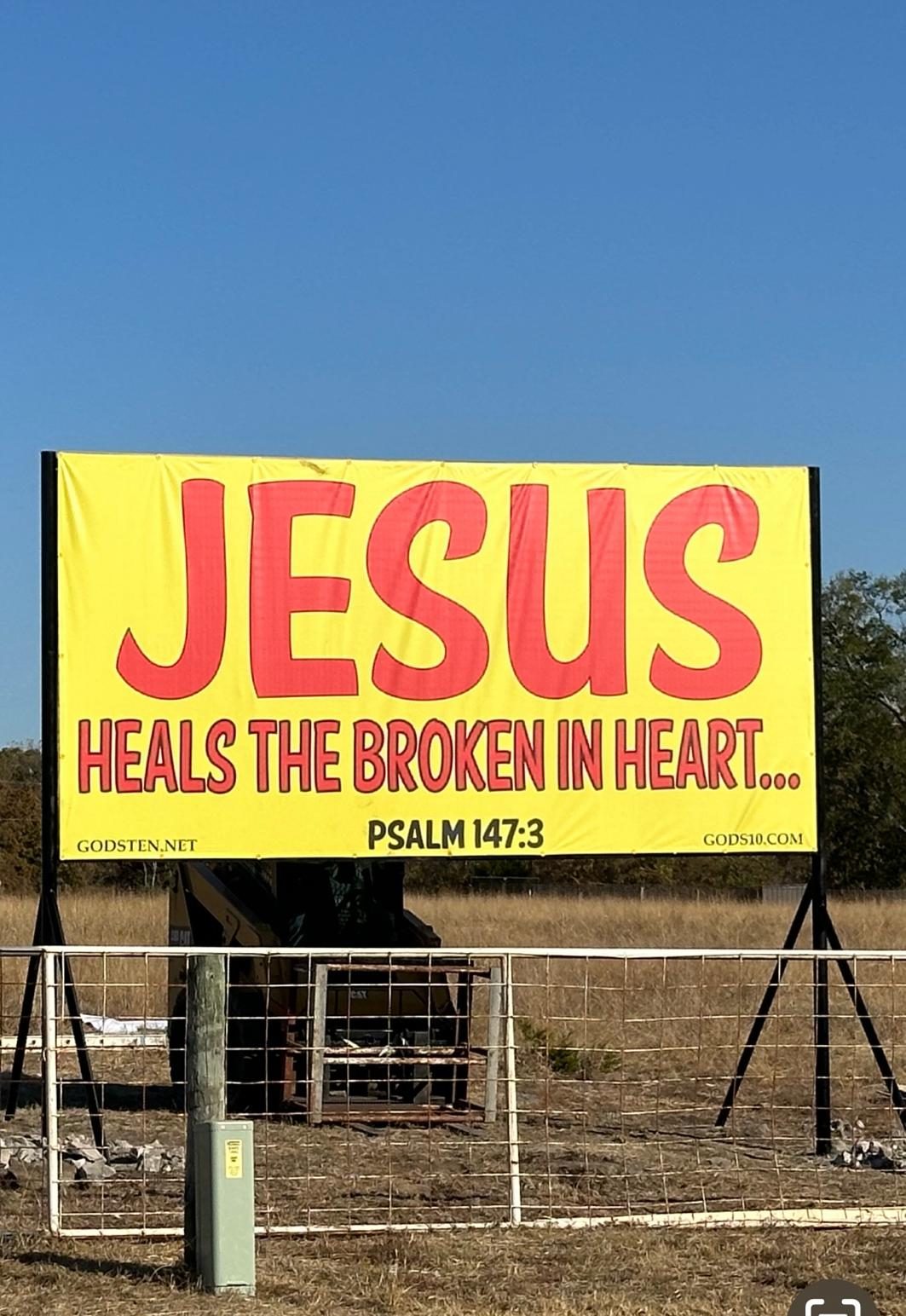 A JESUS heals the broken in heart banner glowing at night beside a country road